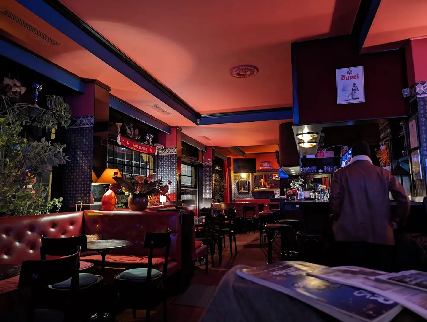 Salle du Pub Lord Jim éclairée de rouge en soirée, banquettes et bar au fond, Pâquis à Genève.