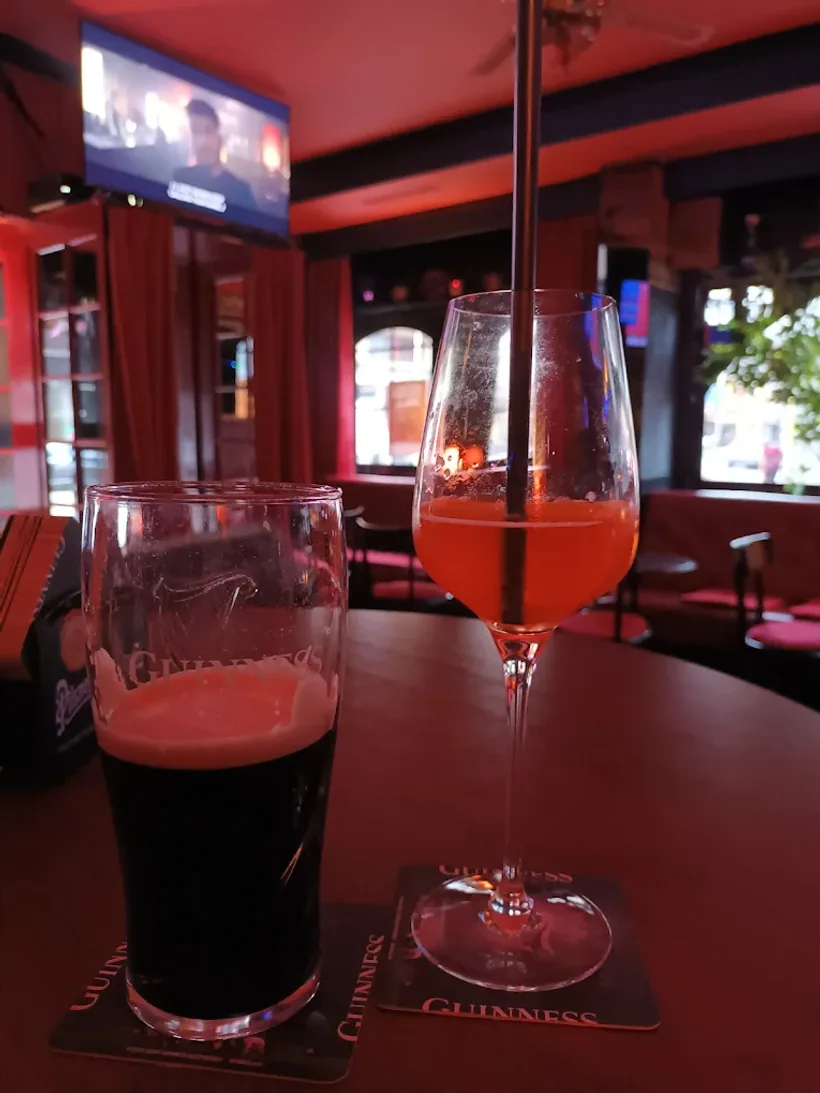 Pinte de Guinness et spritz sur une table du Pub Lord Jim, écran de sport en arrière-plan.
